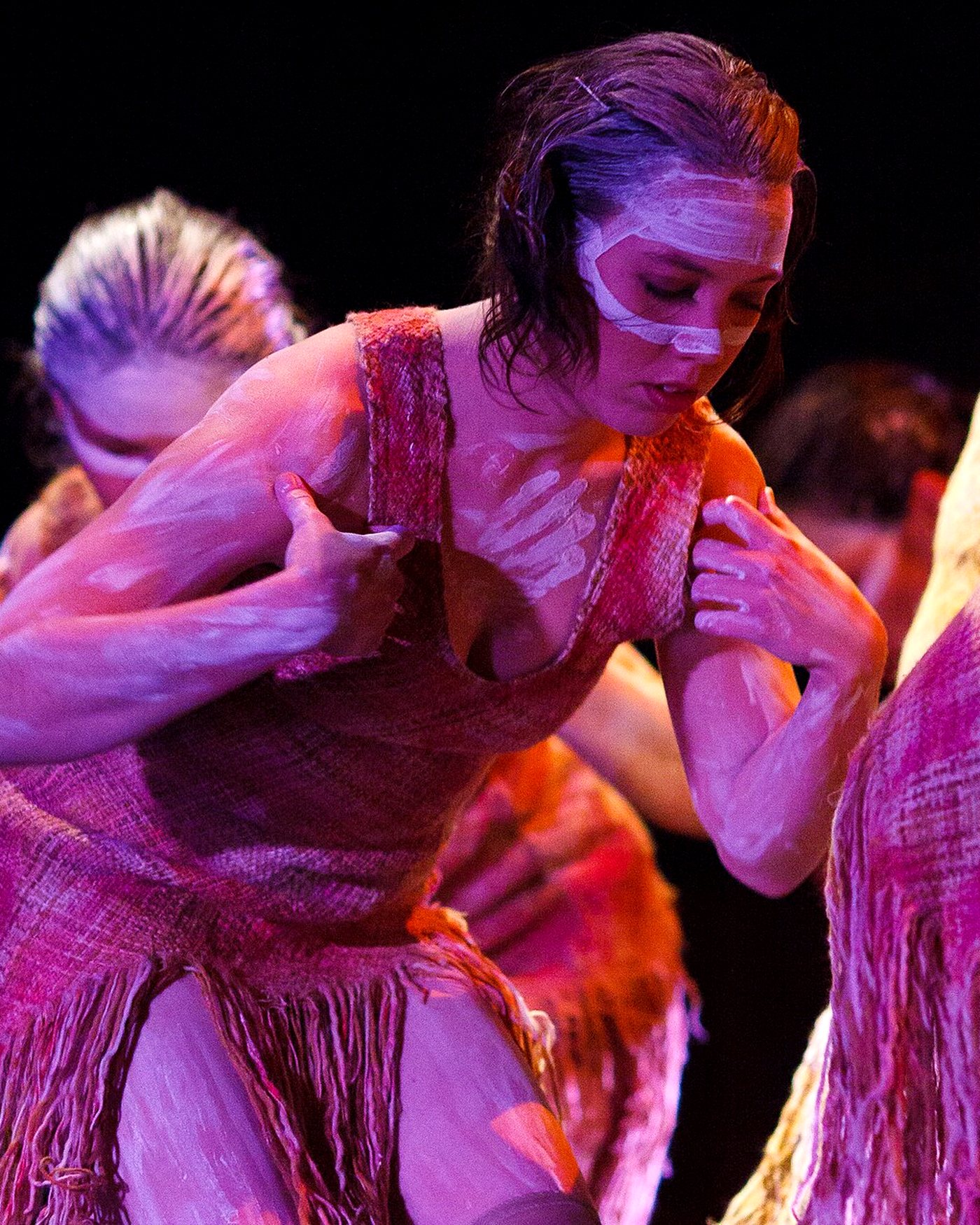 Two dancers close together under magenta light