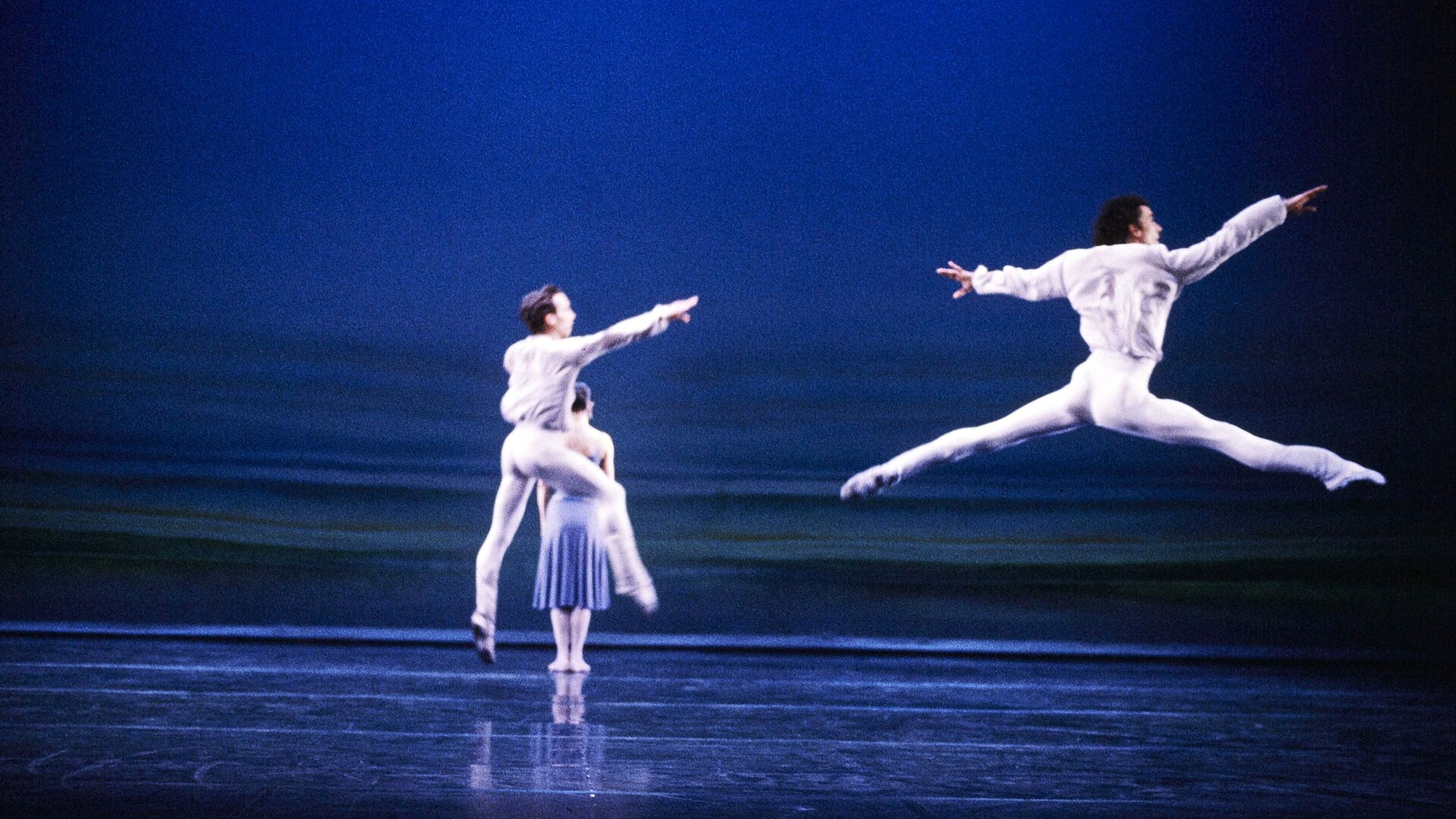 A dancer suspended mid-leap above a stage washed in deep blue light