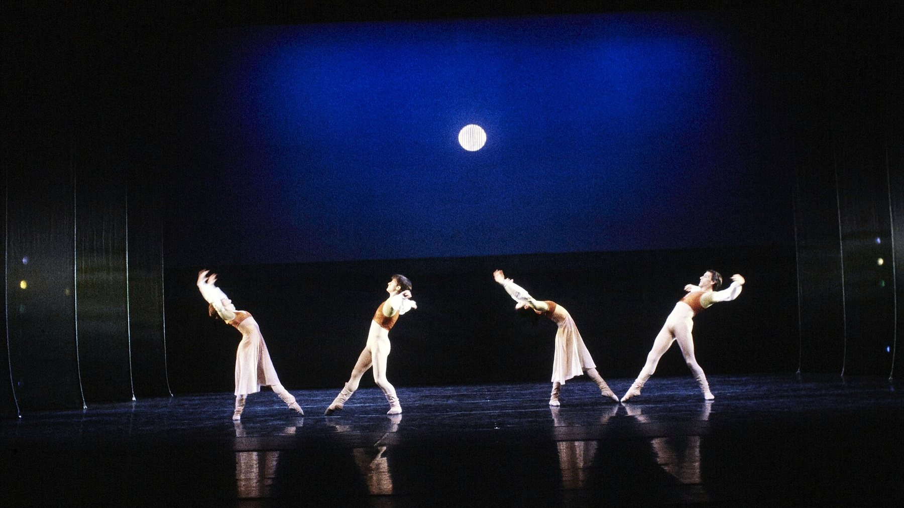 Dancers lined up beneath a white moon suspended over the stage