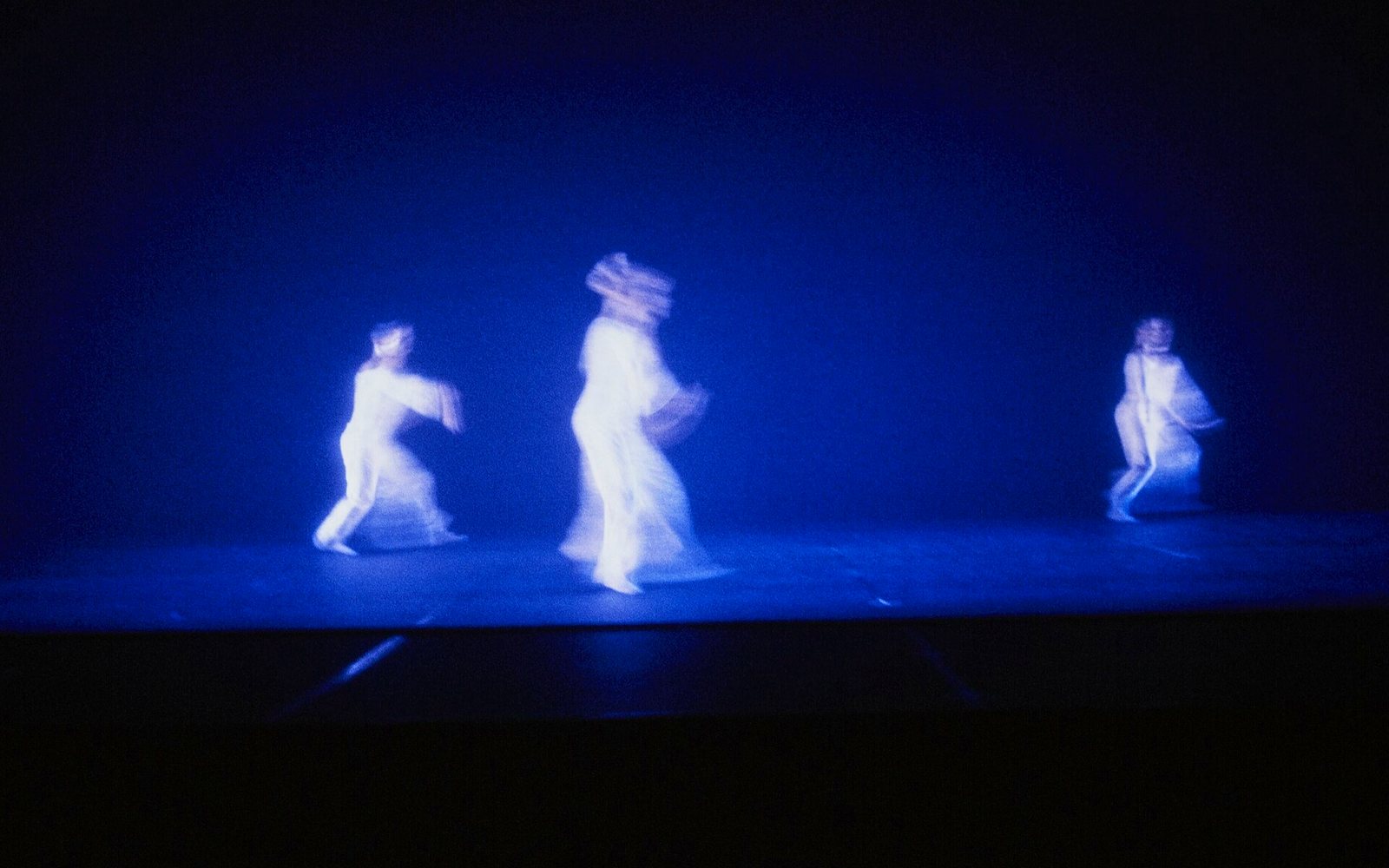 Dancers caught in long exposure, dissolving into a field of deep blue light