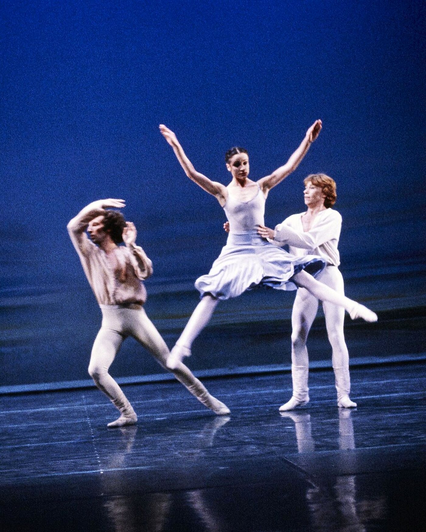 Three dancers in white suspended in a jump