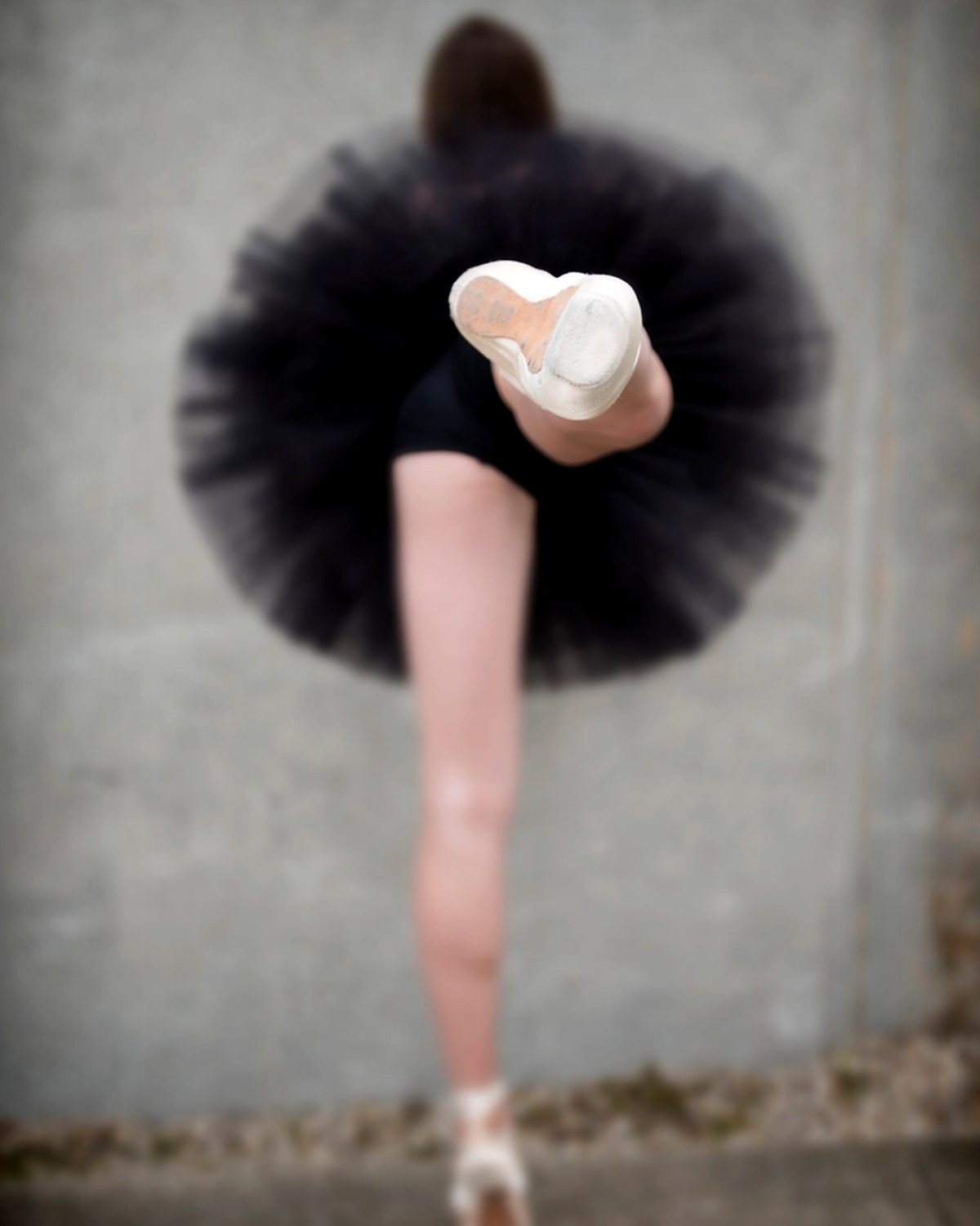 A dancer in a black tutu against a pale wall
